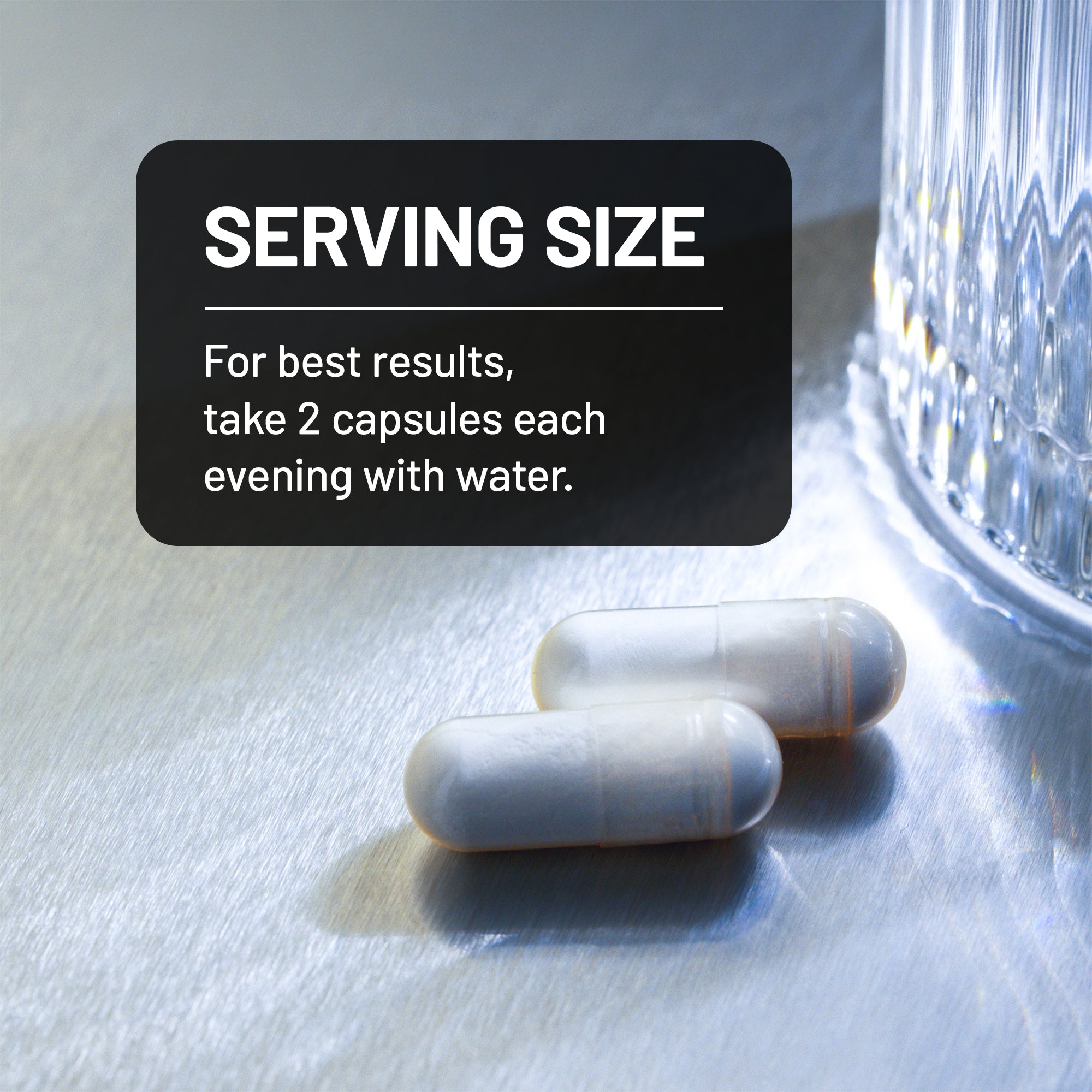Two capsules on a reflective surface with a glass of water in the background and text about serving size.