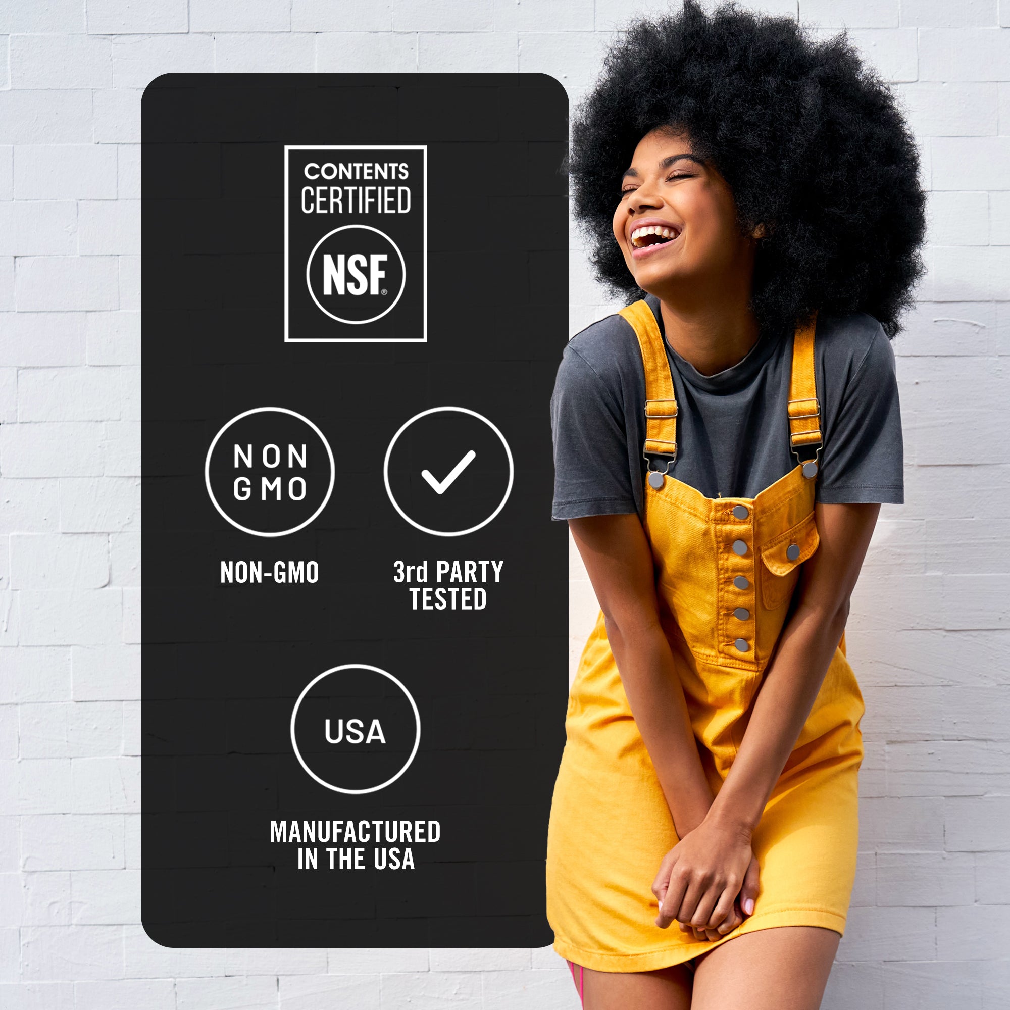 Woman in yellow overalls standing next to a certification label on a white brick wall.