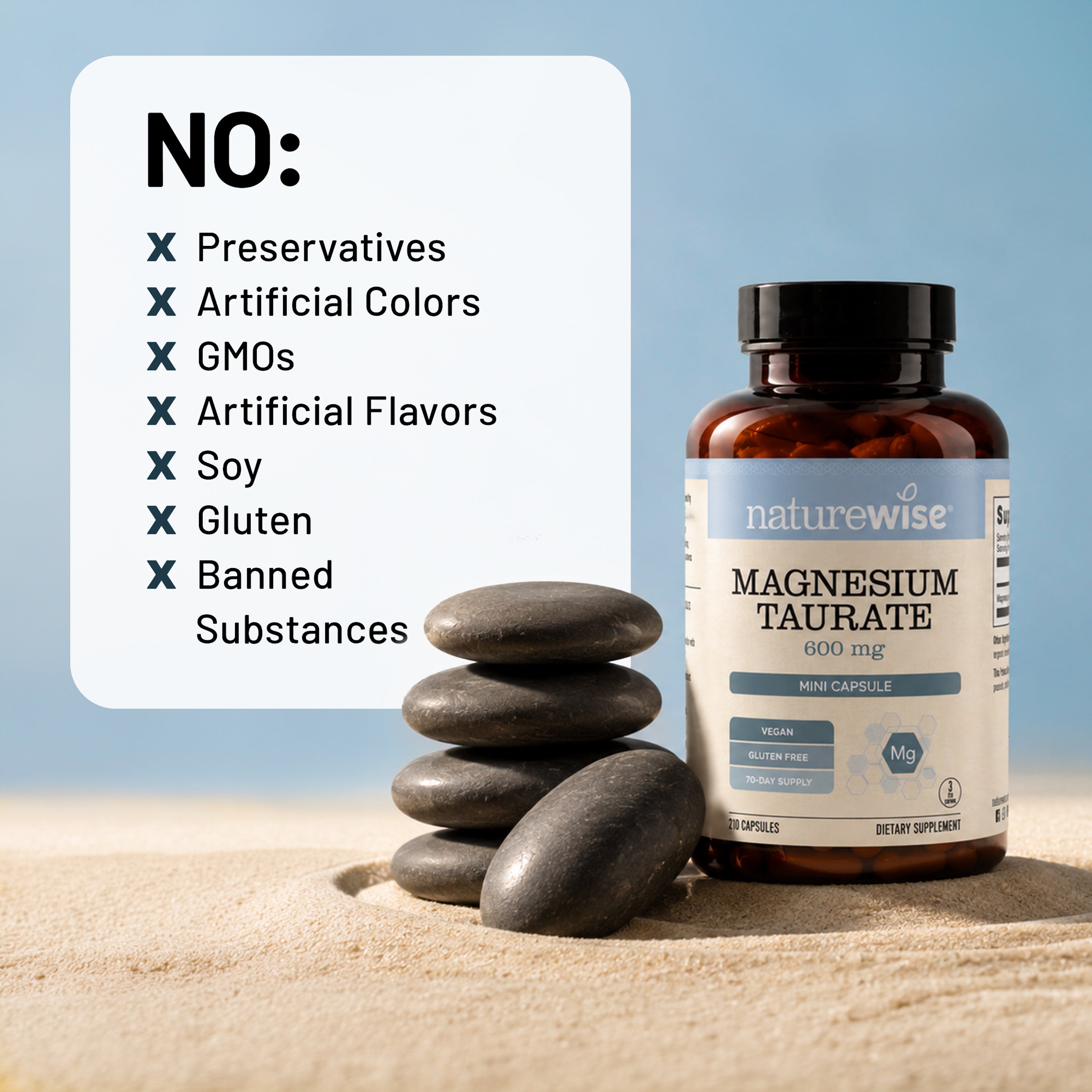A bottle of NatureWise Magnesium Taurate dietary supplement stands on sand next to a stack of smooth dark stones, with a white informational card listing excluded substances like preservatives, artificial colors, GMOs, artificial flavors, soy, gluten, and banned substances.