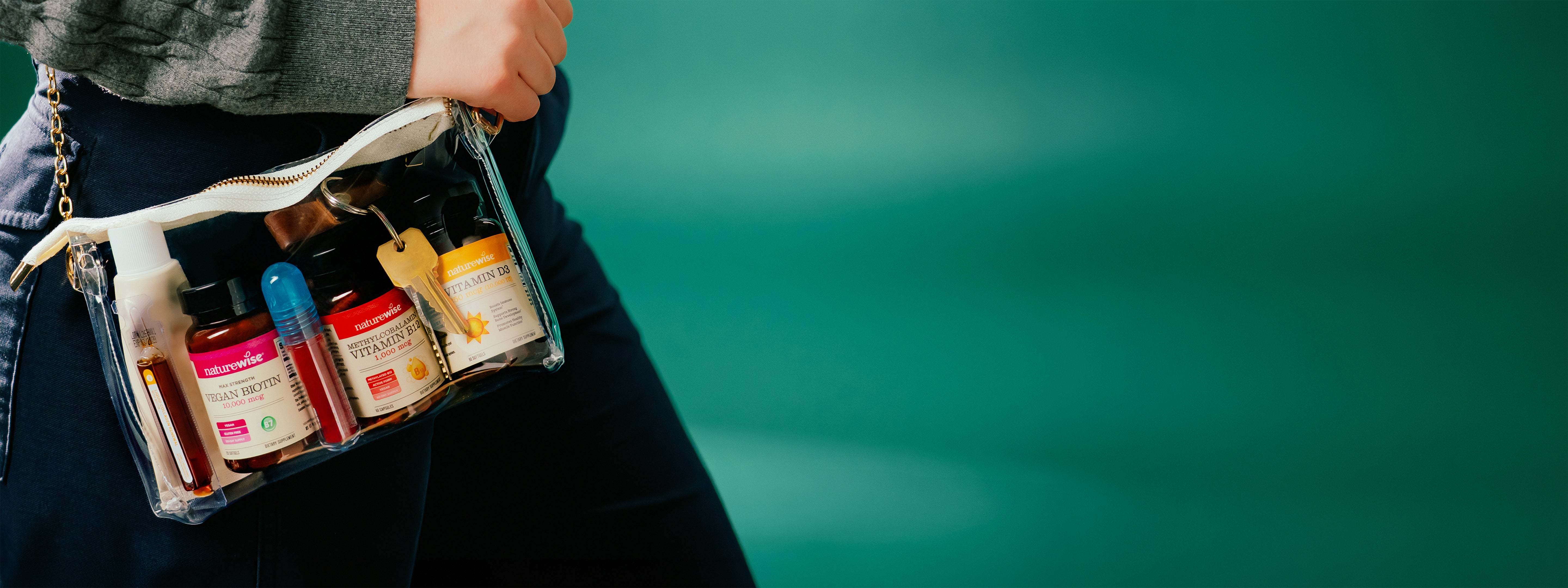 Person holding a transparent bag with various NatureWise supplement bottles against a blurred green background