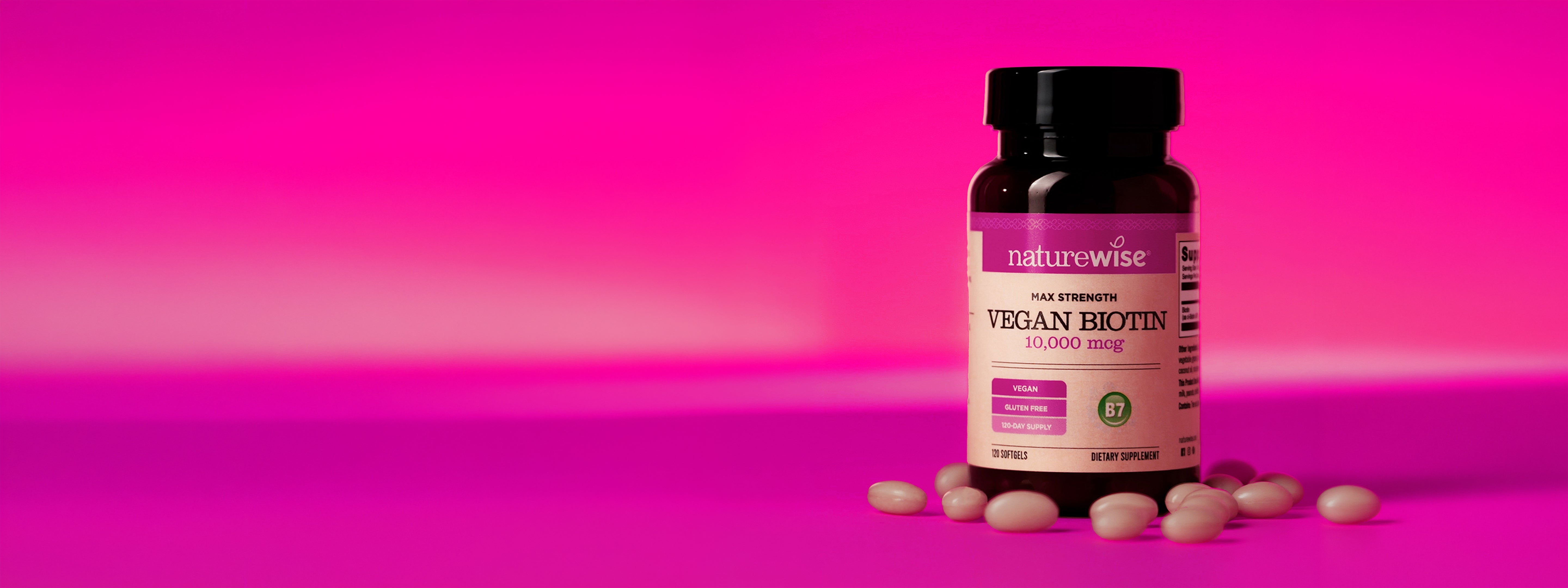 Bottle of NatureWise Vegan Biotin supplement with softgels on a pink background
