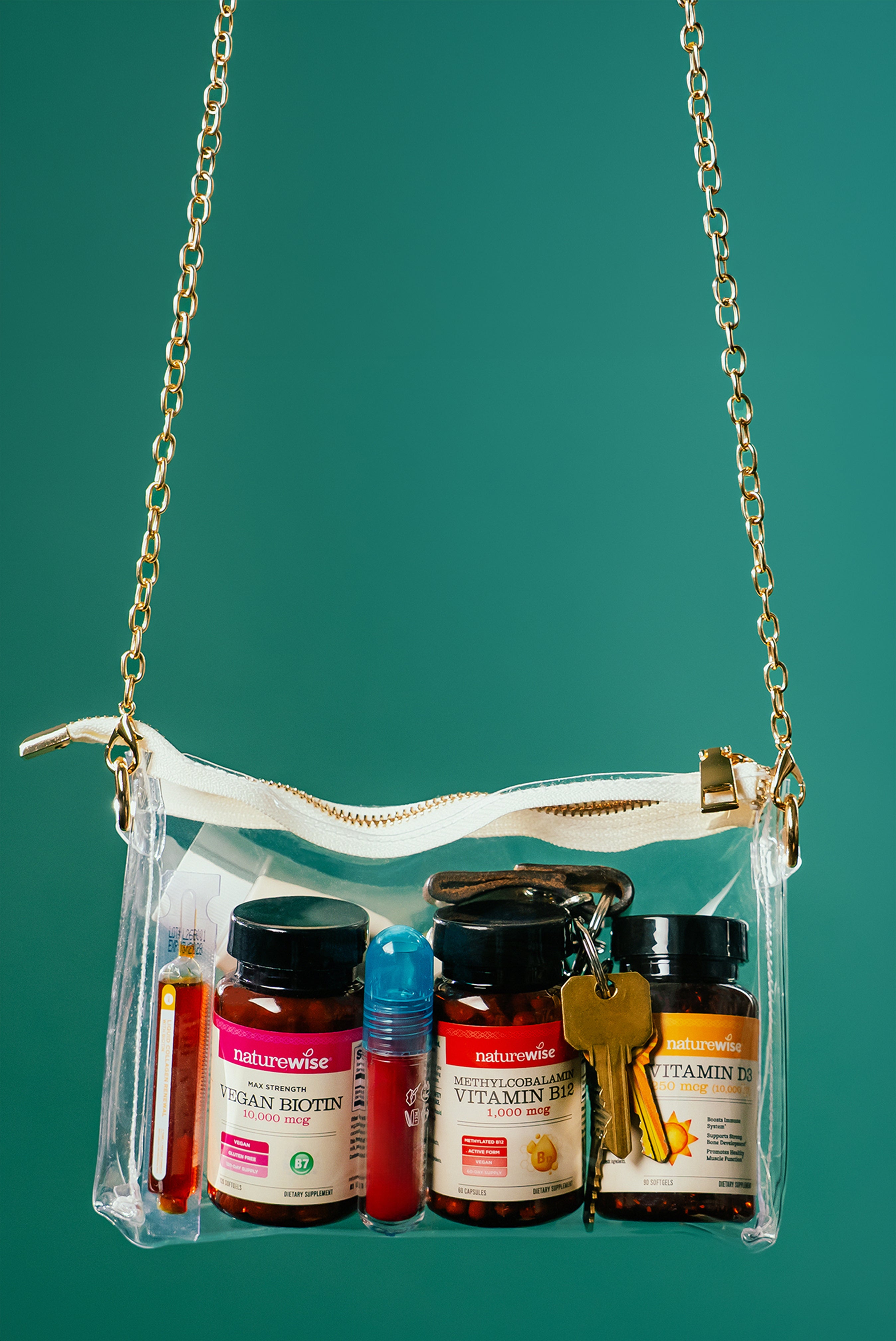 Clear handbag with gold chain strap containing various NatureWise Supplement bottles and keys on a green background
