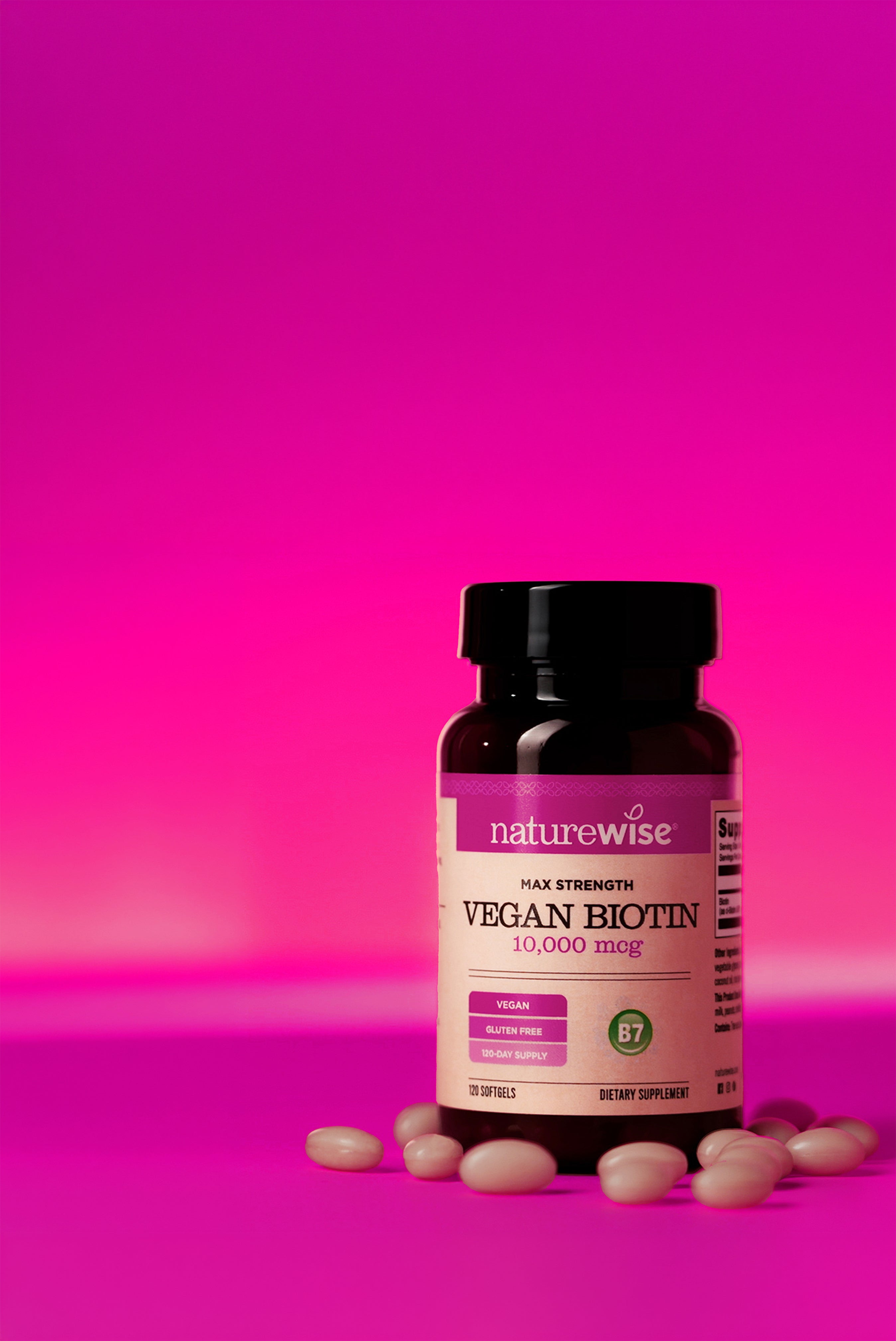 Bottle of NatureWise Vegan Biotin supplement with softgels on a pink background