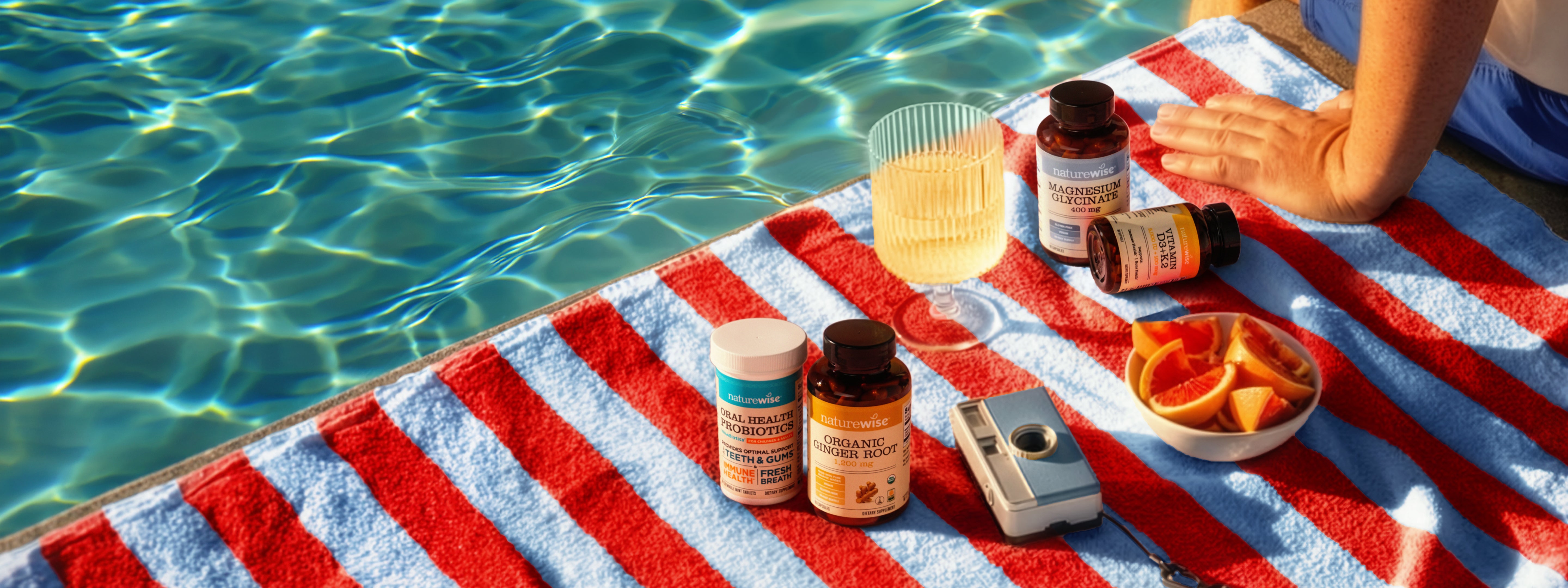 Four NatureWise health supplement bottles arranged on a red and white beach towel by a sunny swimming pool fourth of july.