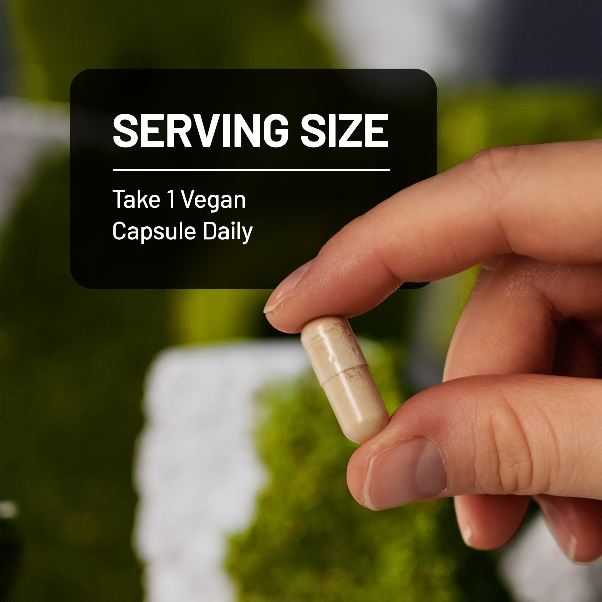 Hand holding a vegan capsule with text overlay on a blurred natural background