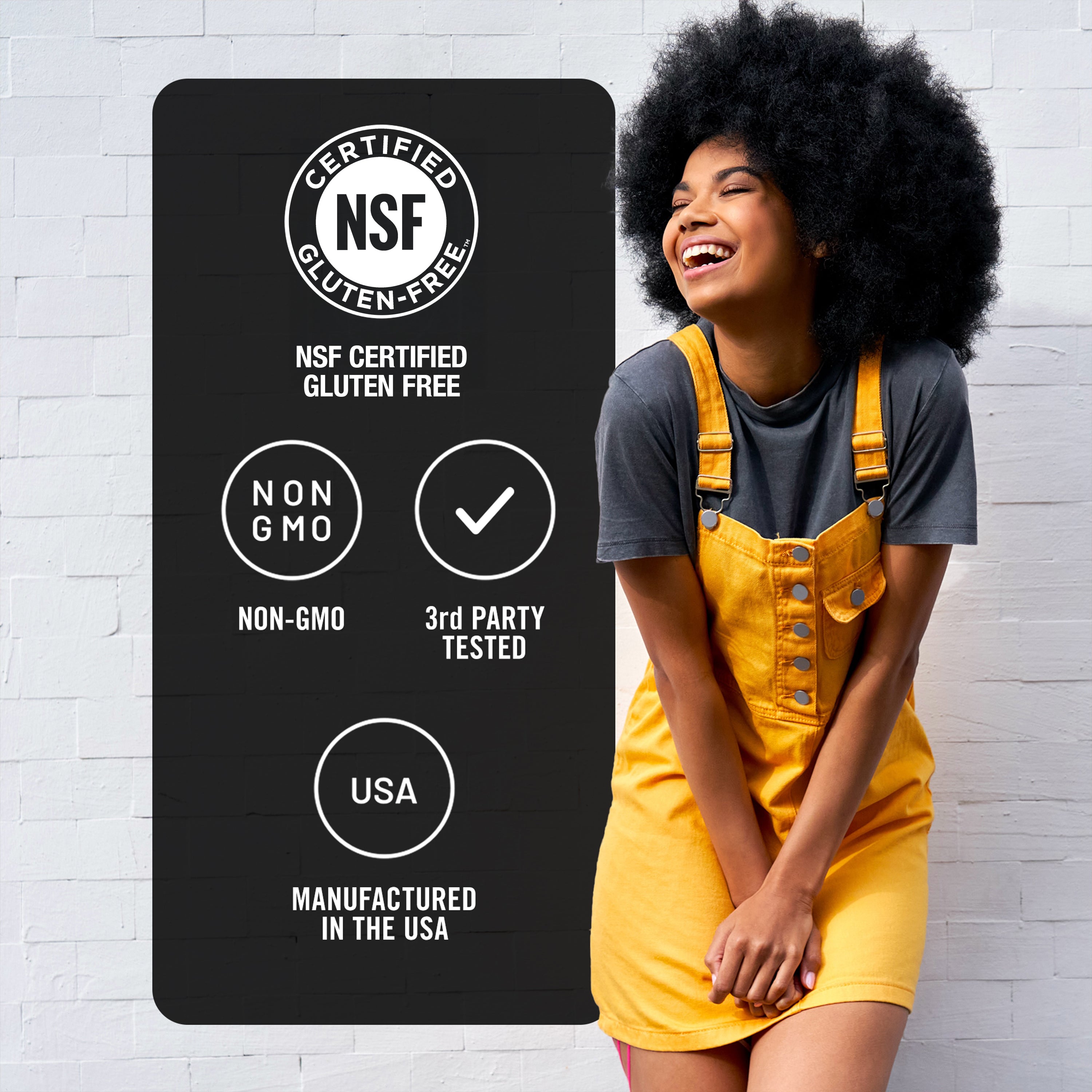 Woman in yellow overalls standing next to a certification label on a white brick wall.