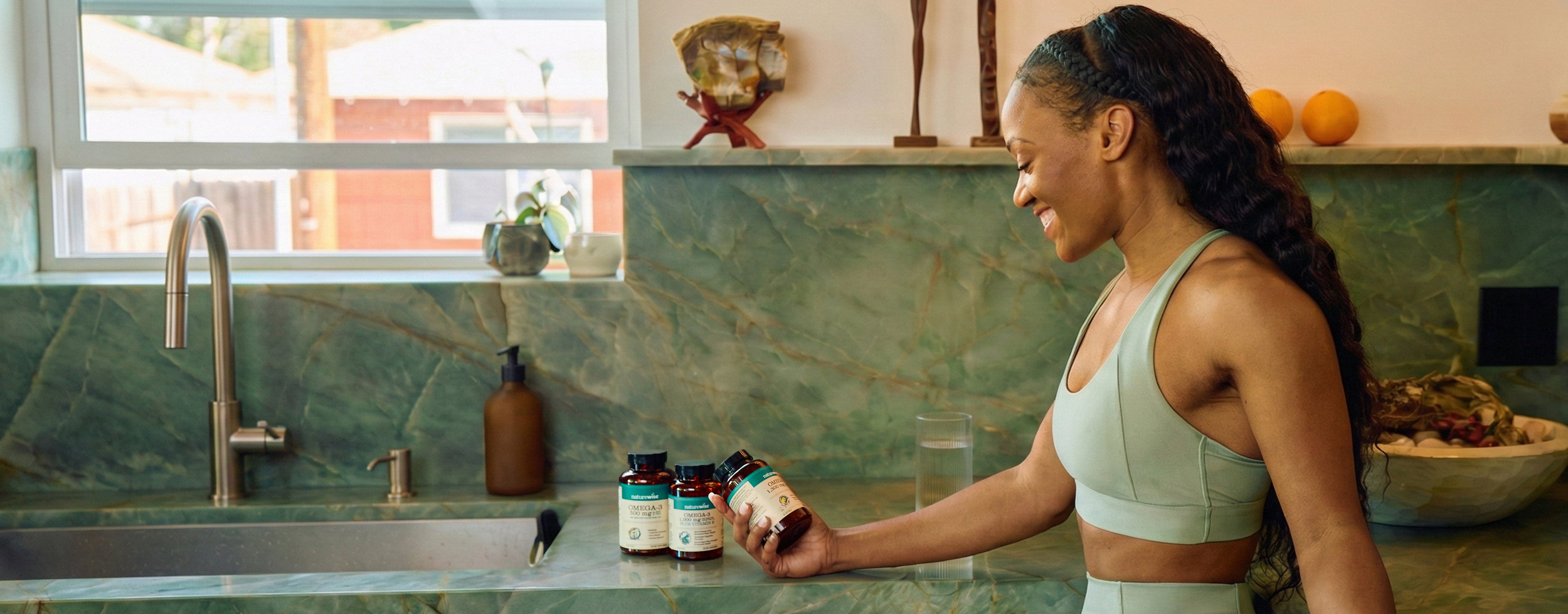 Woman in a kitchen holding a bottle of supplements next to a sink.