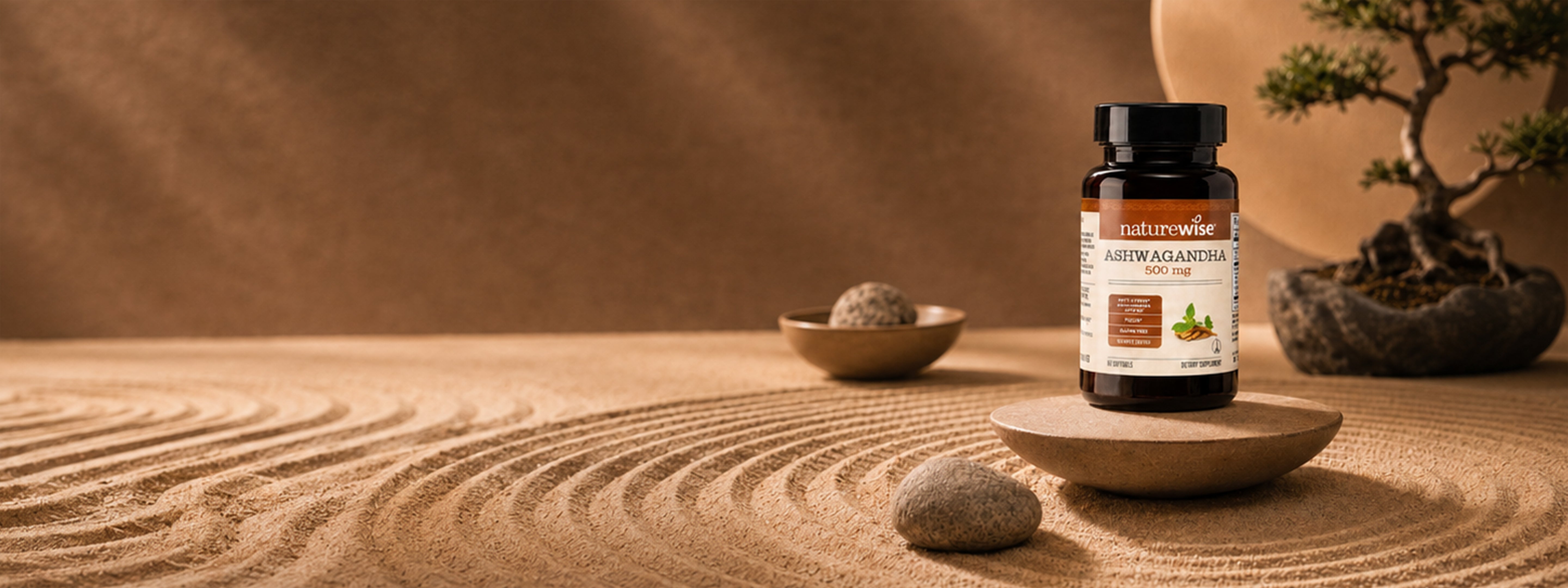 A bottle of Nature's Way Ashwagandha capsules stands on a small wooden dish in a styled zen-like scene with raked sand, stones, bowls, and a bonsai tree against a warm brown background.
