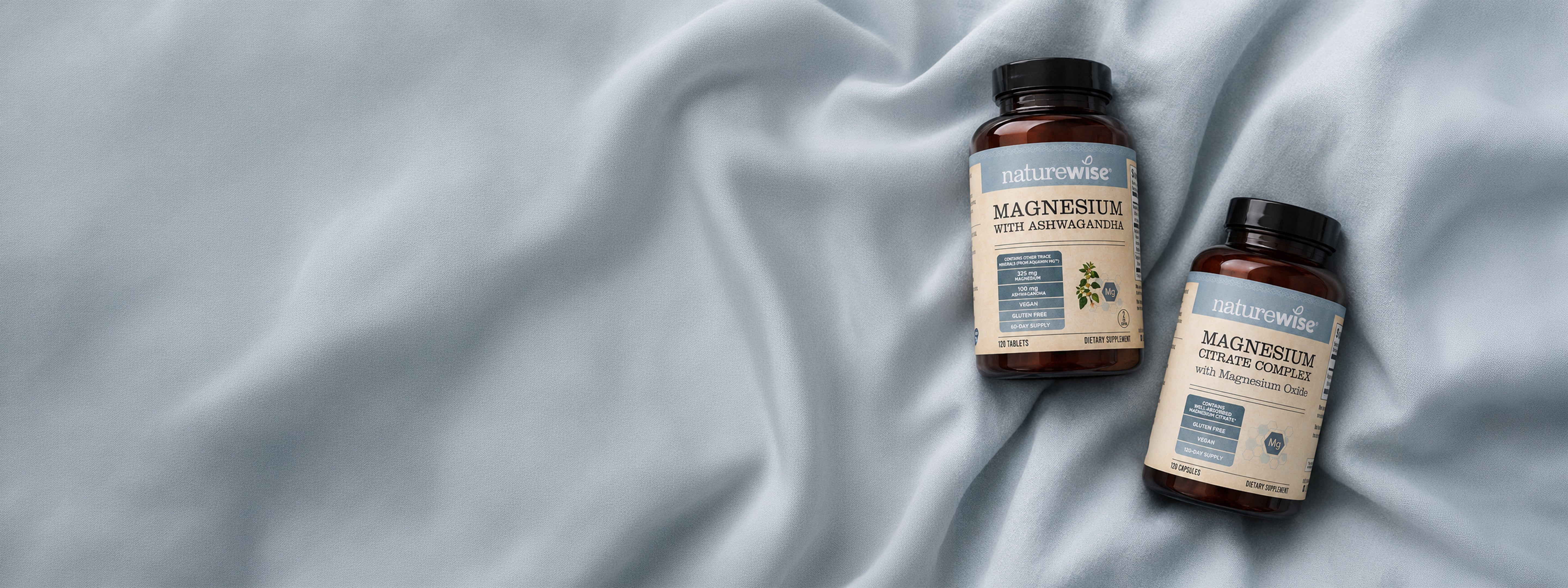 Two amber NatureWise supplement bottleslabels reading NatureWise Magnesium Citrate Complex and Magnesium with Ashwagandha arranged on draped light blue fabric.