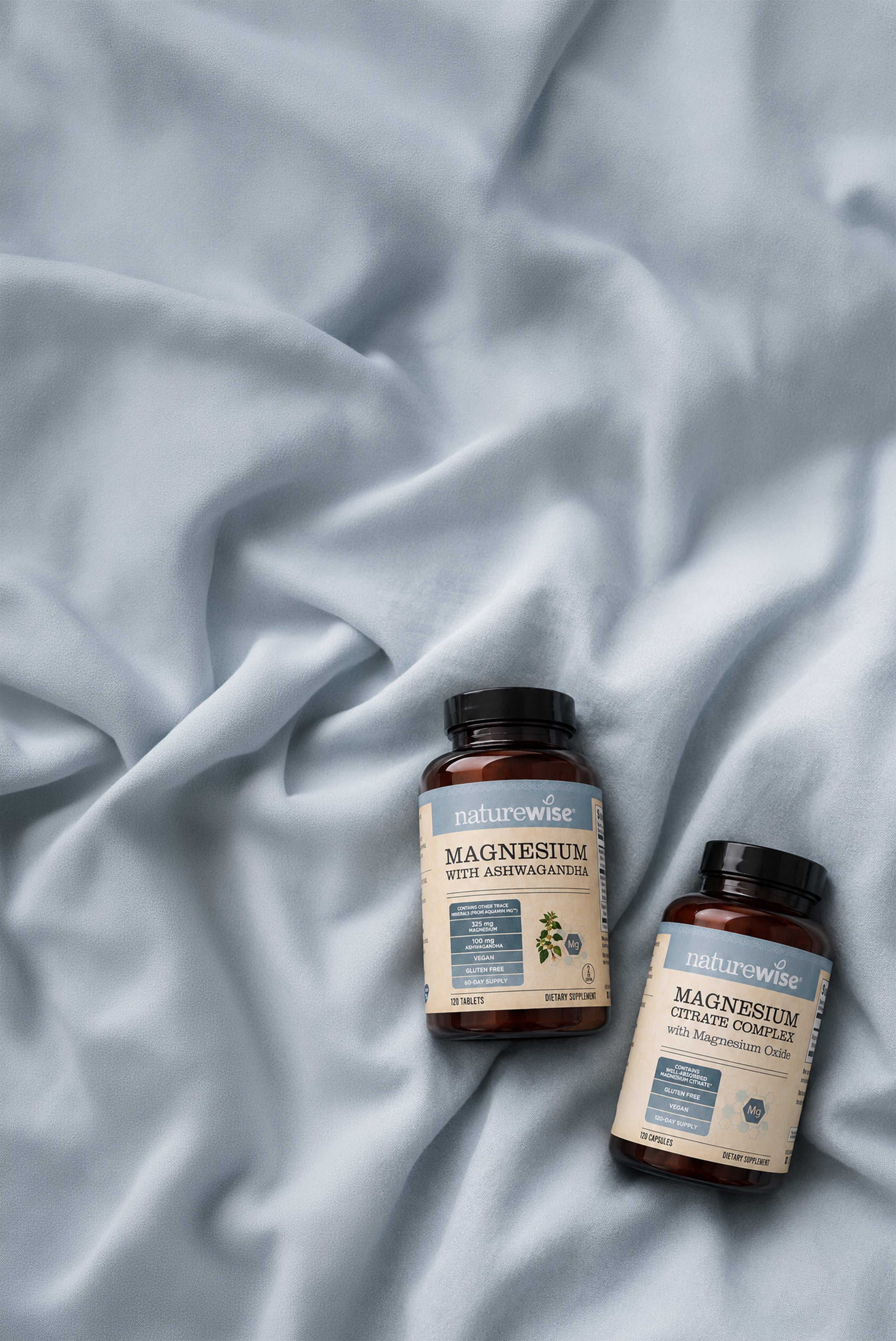 Two amber NatureWise supplement bottleslabels reading NatureWise Magnesium Citrate Complex and Magnesium with Ashwagandha arranged on draped light blue fabric.